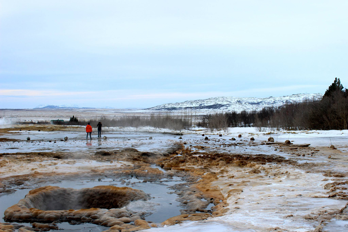 A picture of the geyser located at Geysir in Iceland. Sean and George can be seen in the background